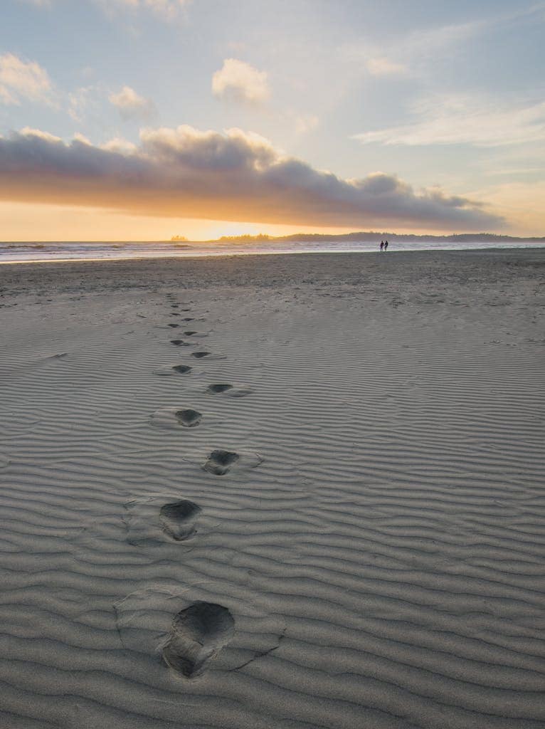 Tranquil beach scene at sunset with footprints leading to the horizon.