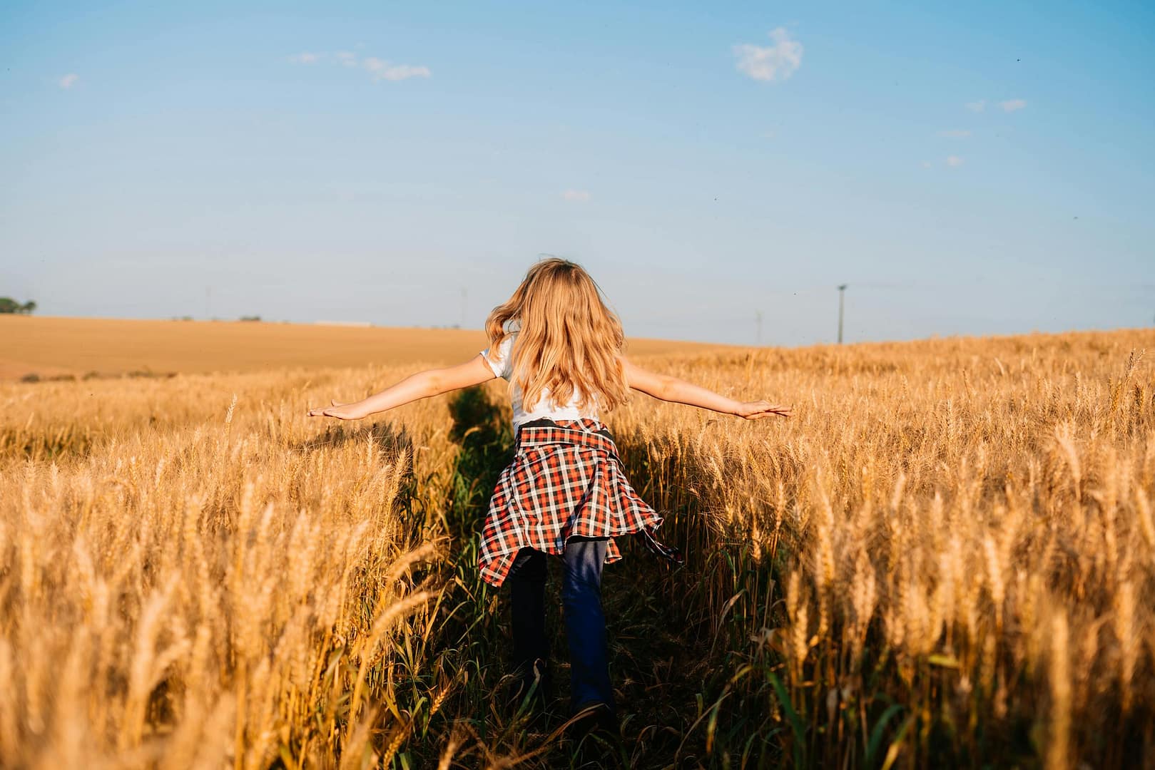 A young girl joyfully runs through a golden wheat field during sunset, evoking freedom and summer vibes.