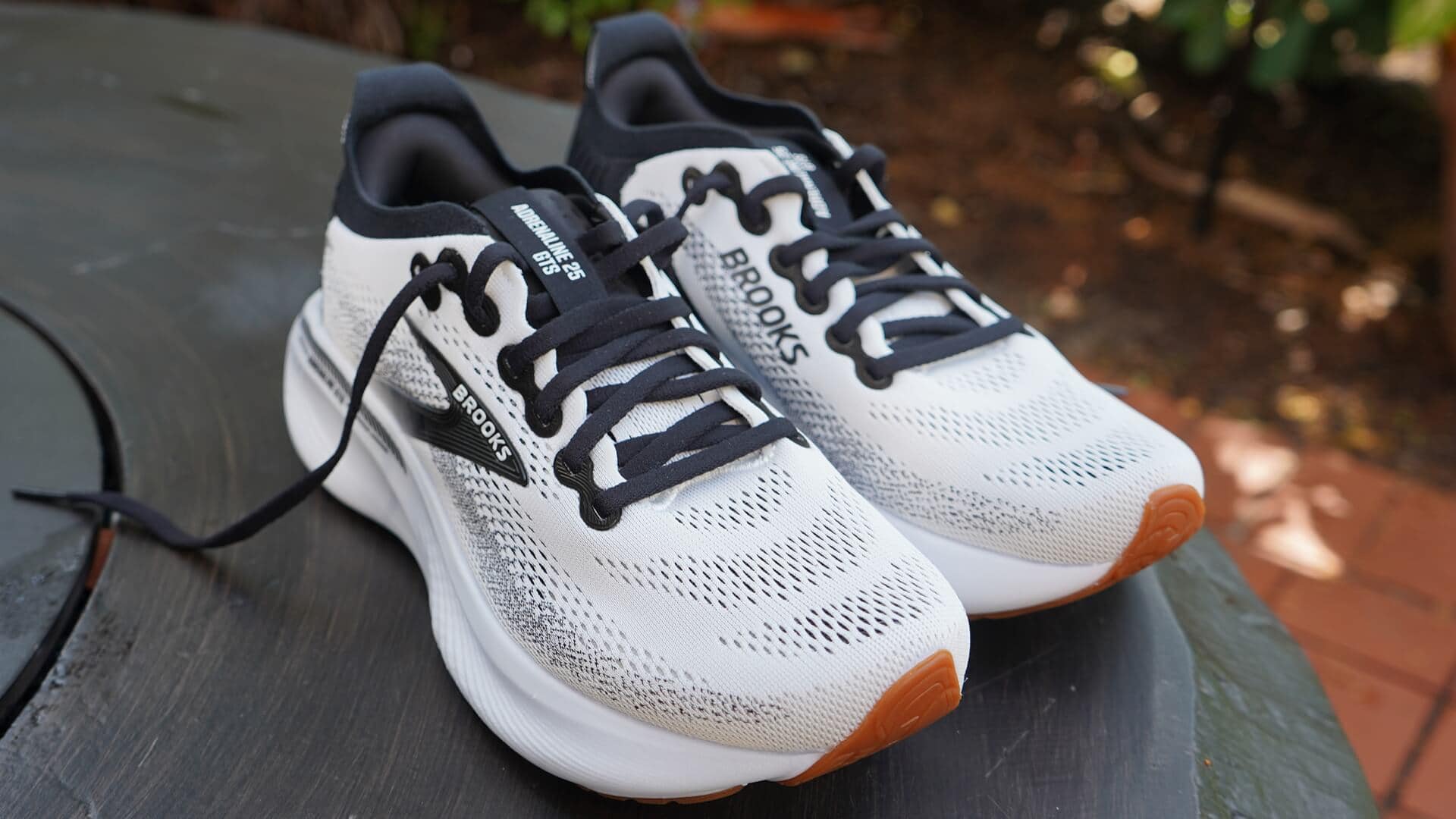 Pair of Brooks Adrenaline GTS 25 walking shoes in White Black White colorway sitting outdoors on a patio table.