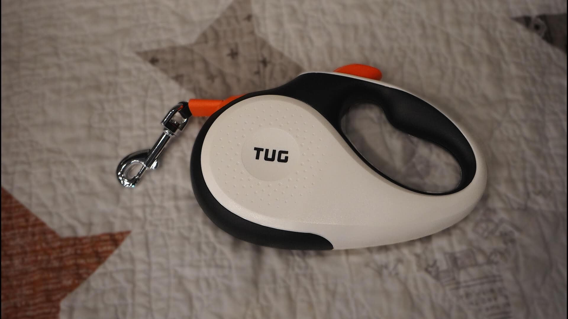 Retractable TUG leash laying on a quilt.