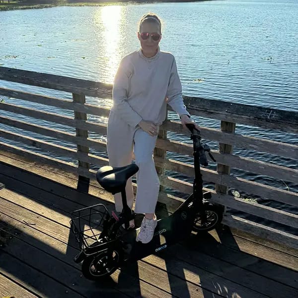 Woman with foot on e-scooter on dock by water.