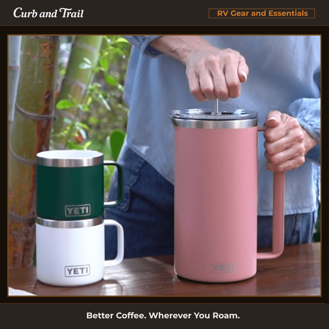 Yeti 64 oz French press and two yeti mugs outdoors with hand pressing down on French press.